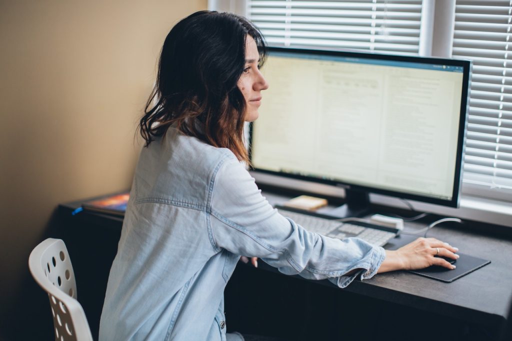 This image shows a woman sitting at a desk in front of a desktop computer.