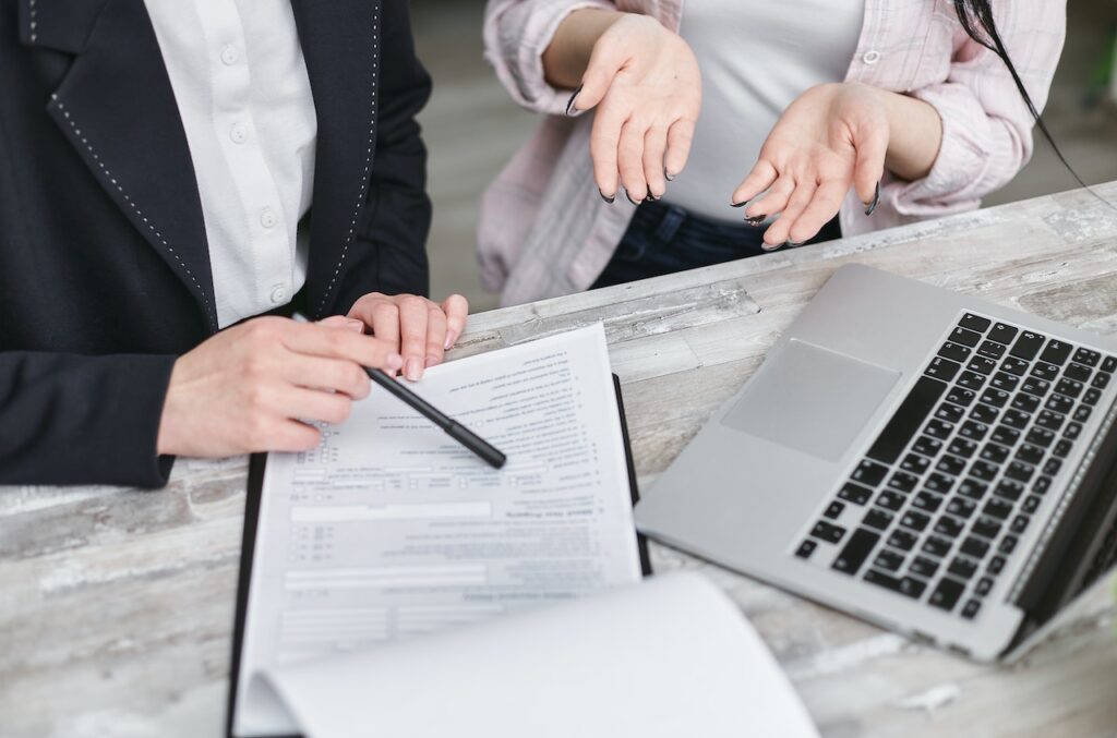 This image shows two people sitting at a desk with a laptop and a report on its surface.