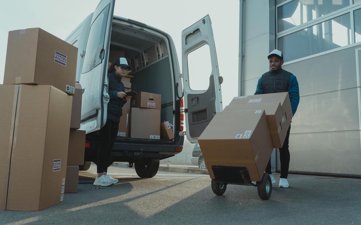 Workers loading boxes into a van with a trolley.